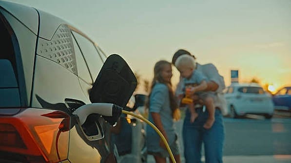 Electric car charging at sunset while a family talks nearby